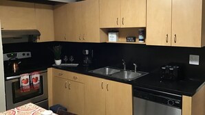 A kitchen with wooden cabinets, a black countertop, a coffee machine, a sink, and a dishwasher. - Modern 3/1 house near Beaches and Midtown (Miami)