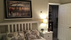 A bedroom with a bed, a nightstand, a lamp, a framed picture on the wall, and a door leading to another room. - Modern 3/1 house near Beaches and Midtown (Miami)