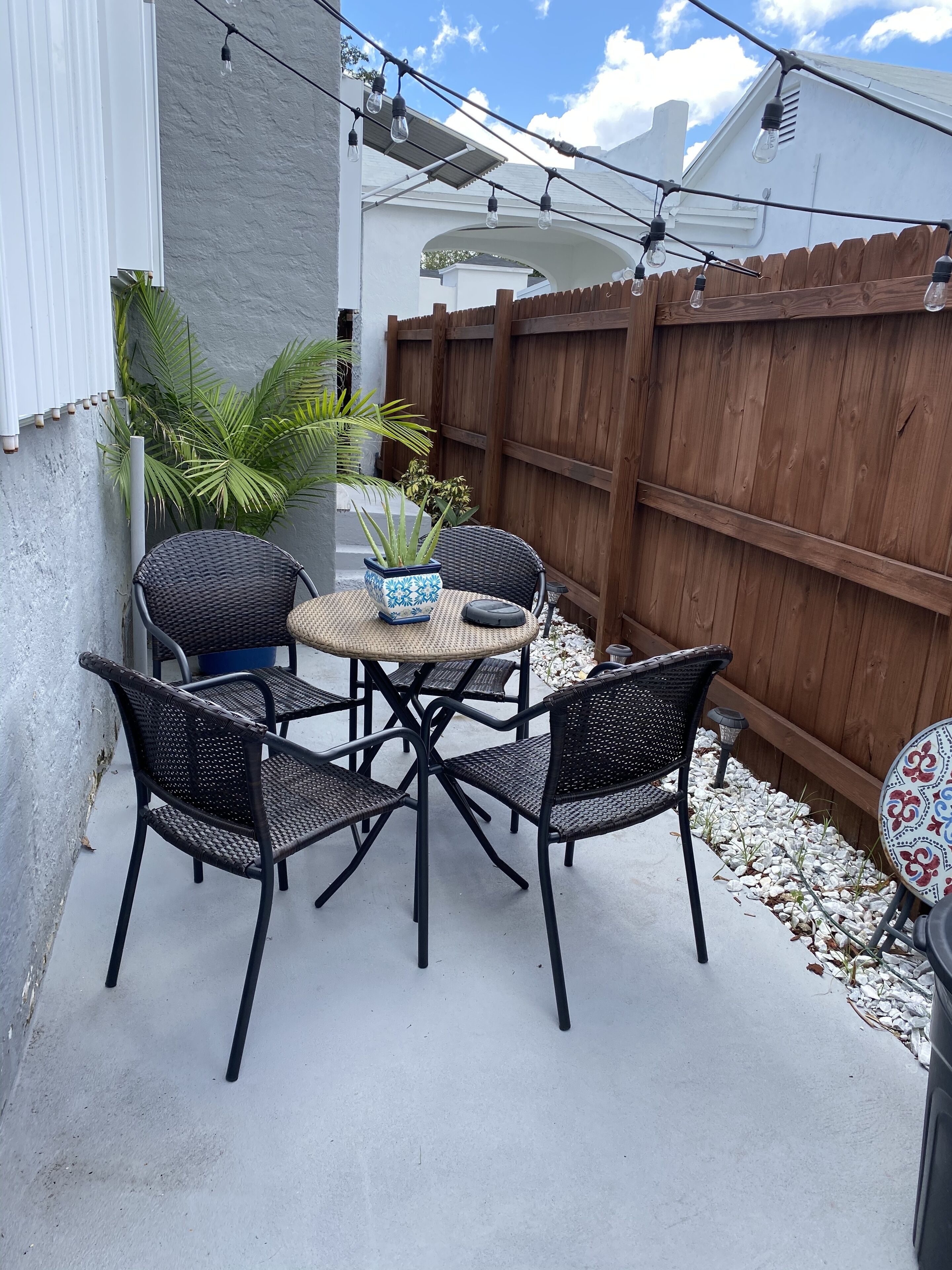 A patio with a round table and four chairs, surrounded by a wooden fence and a white wall.