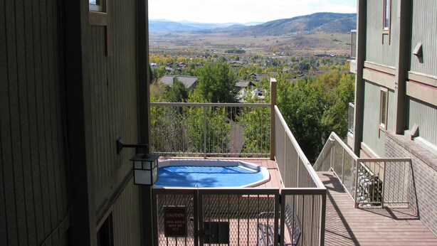 A balcony with a hot tub overlooking a residential area and distant mountains. - Mountain Condo For All Season Fun And Relaxation/ Family Friendly 2Bath2Bedrooms (Steamboat Springs)