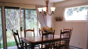 A dining area with a wooden table and chairs, a chandelier, and a view of trees through large windows. - Mountain Condo For All Season Fun And Relaxation/ Family Friendly 2Bath2Bedrooms (Steamboat Springs)