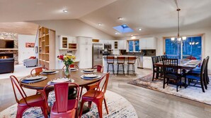 A spacious kitchen with white cabinets, a central island with bar stools, and a dining area with red chairs. - Spacious Home, 2 Living Areas, Jacuzzi Hot Tub, Mountain Views, & Close to Town! (Breckenridge)