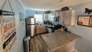 A compact kitchen with wooden cabinets, a stainless steel refrigerator, and a granite countertop.