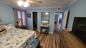 A bedroom with a bed, a ceiling fan, a dresser, a mirror, and a TV.