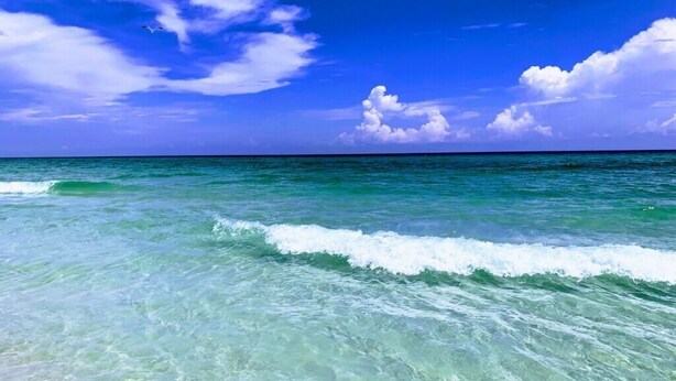 A clear view of turquoise ocean water with gentle waves and a bright blue sky with scattered clouds.