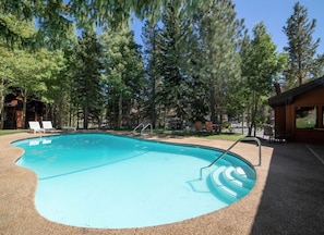 A swimming pool with a curved edge, surrounded by trees and a building with a chimney. - Walk To The Slopes!!! (Mammoth Lakes)