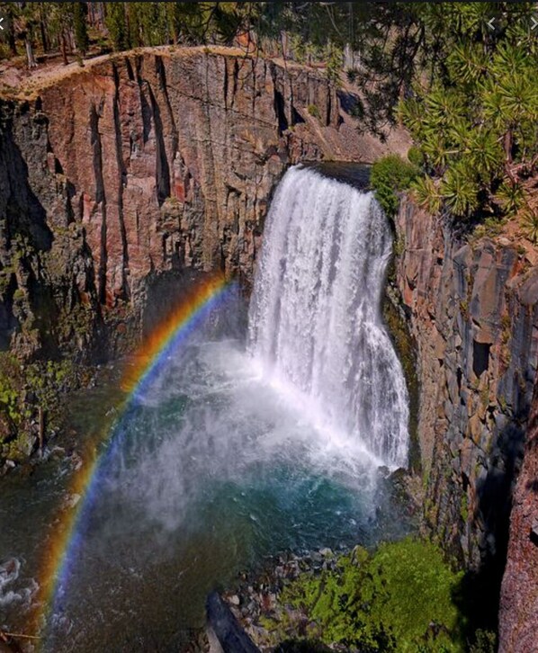 A waterfall cascading down a rocky cliff with a rainbow visible in the mist. - Walk To The Slopes!!! (Mammoth Lakes)
