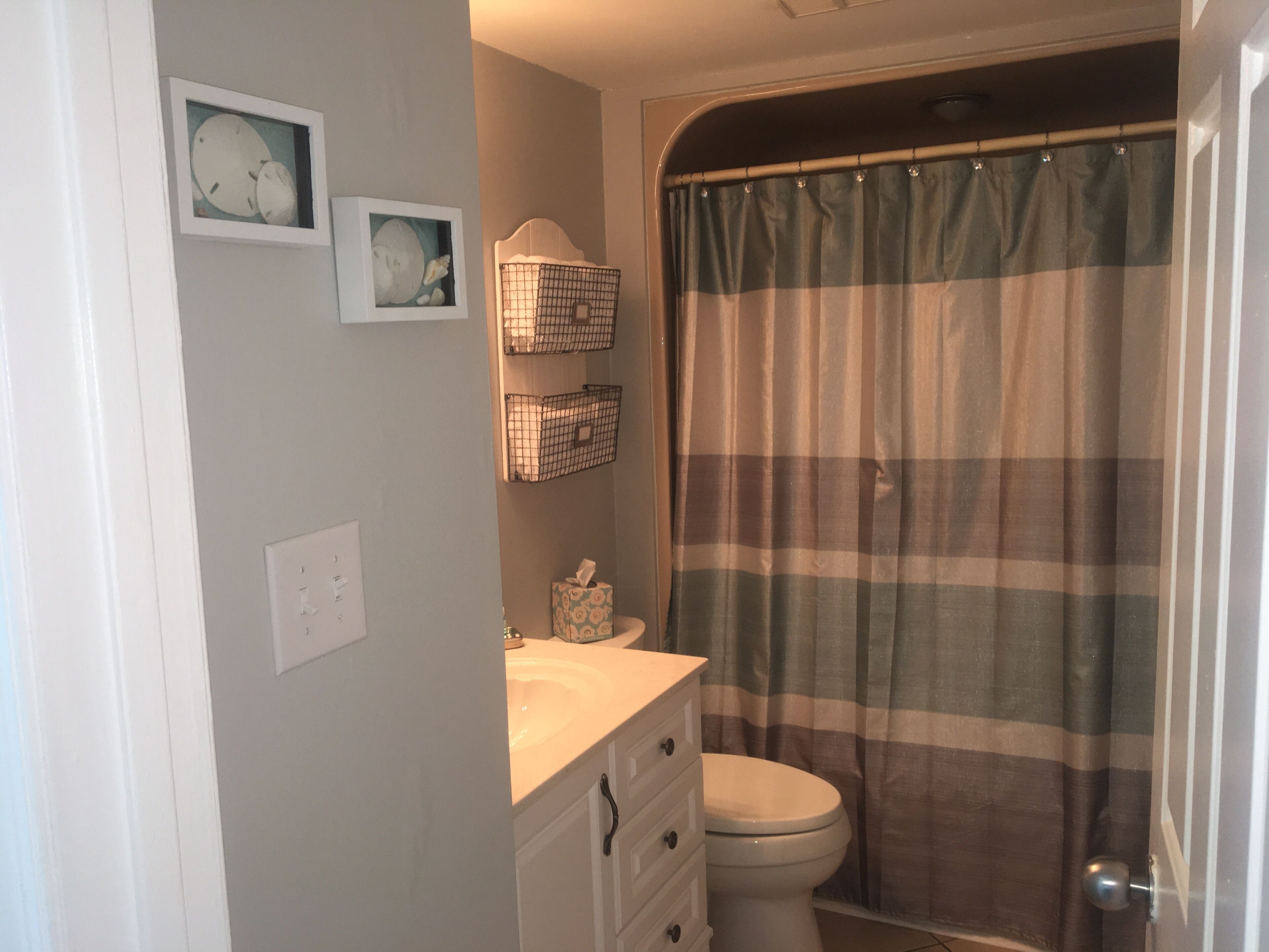 A bathroom with a toilet, a sink, and a shower curtain. There are two wall-mounted baskets above the sink.
