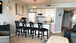 Una cocina moderna con armarios blancos, una isla central y un comedor con cuatro sillas.