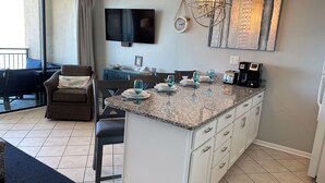 Una cocina moderna con encimera de granito, armarios blancos y una zona de comedor con mesa y sillas.