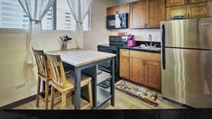 Una cocina compacta con armarios de madera, un refrigerador de acero inoxidable, un microondas y un comedor con mesa y sillas.