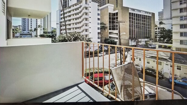 Un balcón con vistas a un paisaje urbano, que incluye edificios altos y una calle con automóviles.