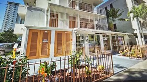 Un hotel de varios pisos con balcones, un jardín cercado y un cartel que indica alta tensión.