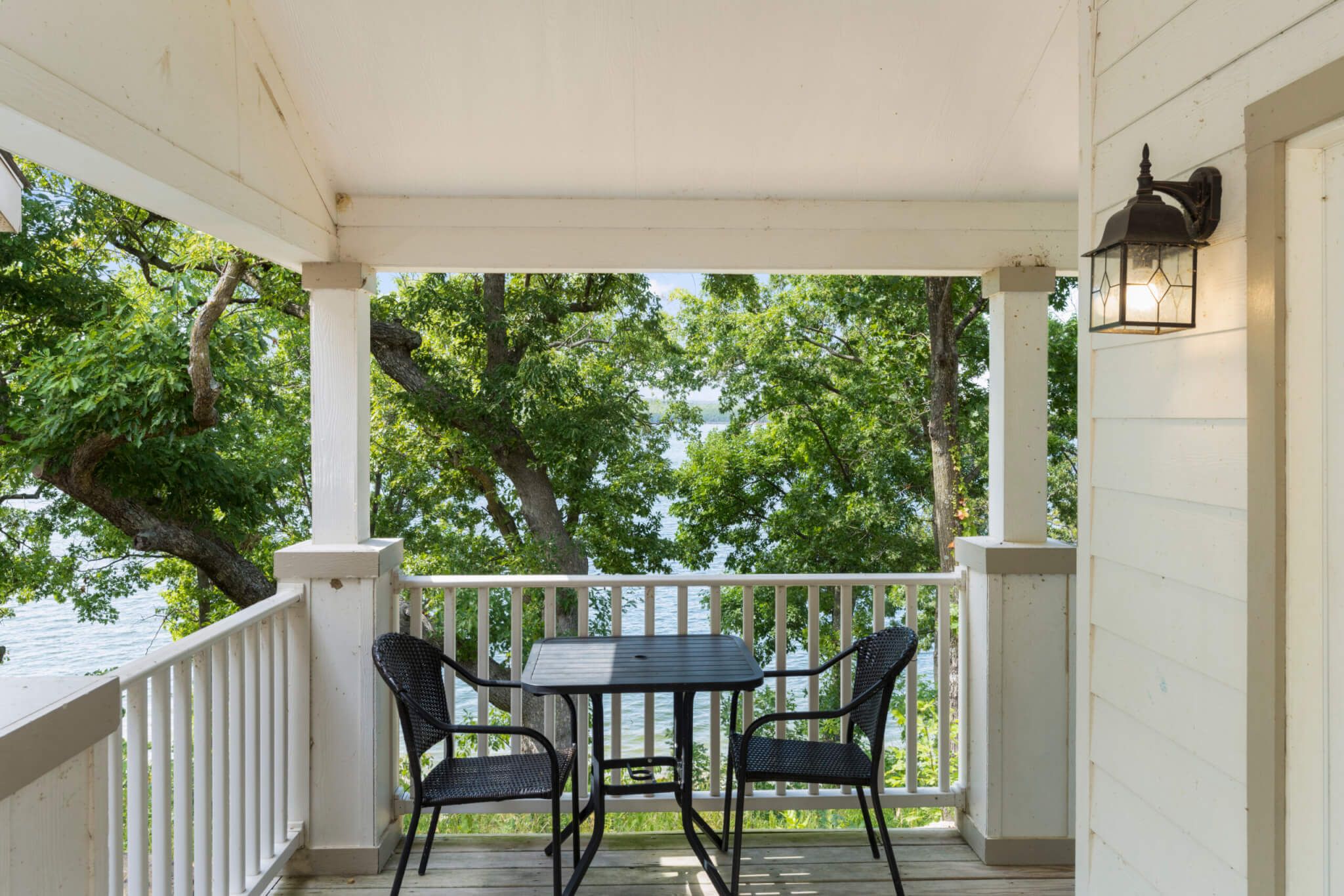 A covered porch with a table and chairs, overlooking a body of water and trees.