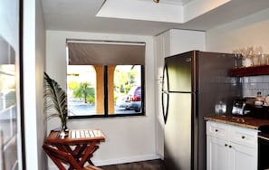 Eine kleine Küche mit Kühlschrank, einem Fenster mit Blick auf die Straße, einem Holztisch und einem Blumentopf.