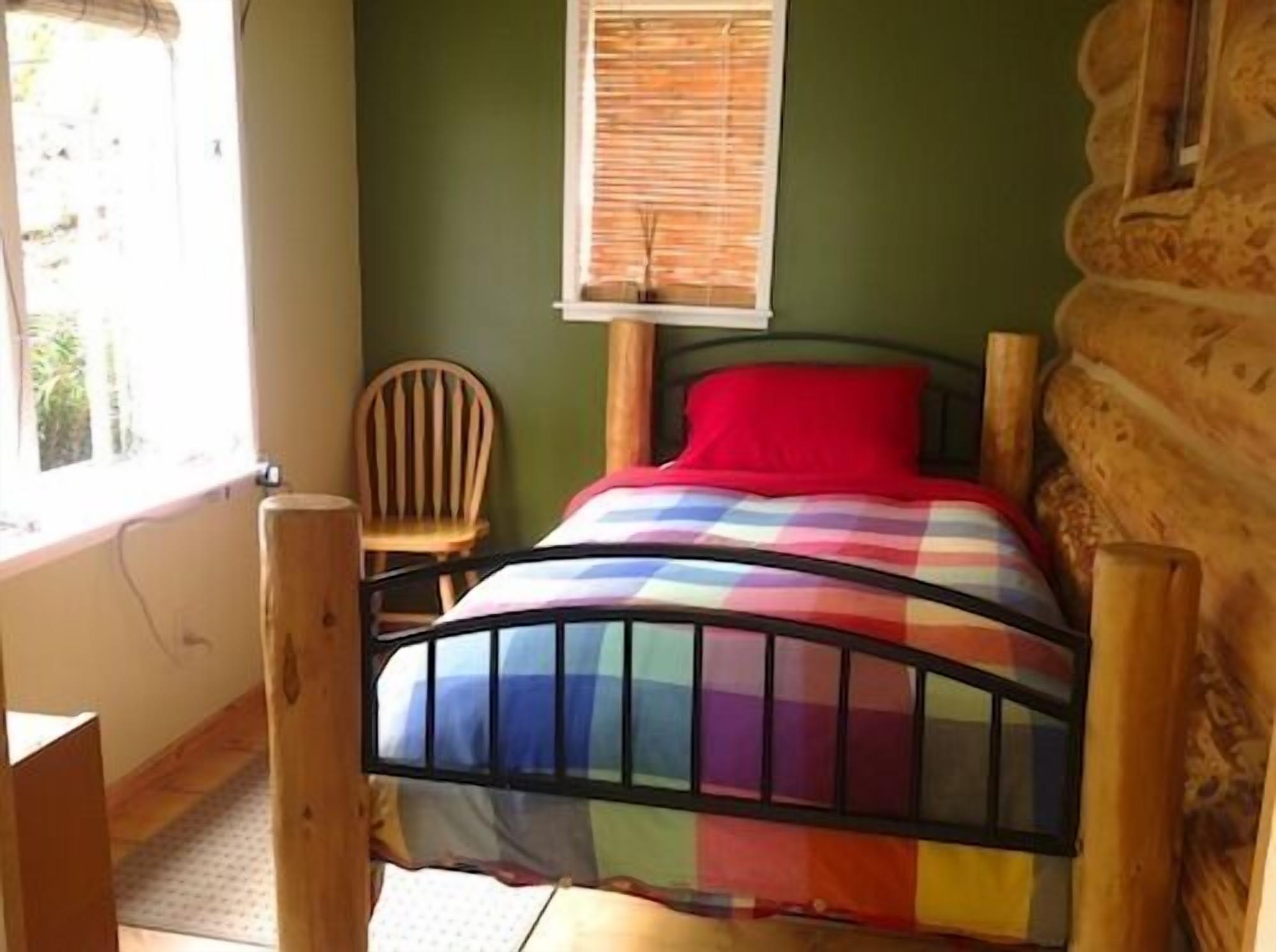 Una habitación con una cama, una ventana con persianas, una silla y suelo de madera.