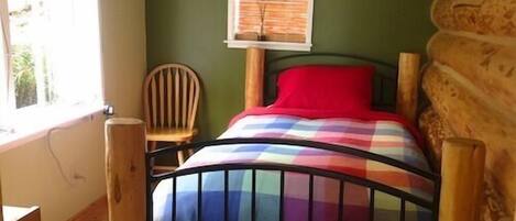Una habitación con una cama, una ventana con persianas, una silla y suelo de madera.