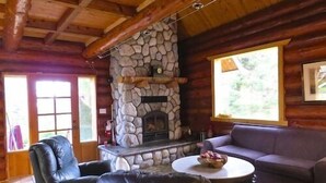 A log cabin interior with a stone fireplace, leather furniture, and a large window.