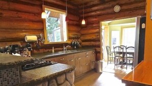 A log cabin interior with a stone island counter, wooden cabinets, a sink, and a dining area with chairs.