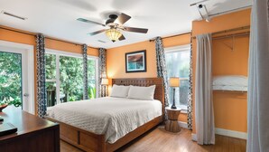 A bedroom with a wooden bed, a ceiling fan, and a view of greenery through large windows. - Great Family Beach House and 5% off weekly stays, last minute or mobile booking! (Folly Beach)