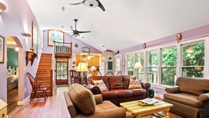 A spacious living room with a staircase, leather sofas, wooden flooring, and large windows. - Great Family Beach House and 5% off weekly stays, last minute or mobile booking! (Folly Beach)