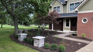 A two-story house with a brick facade, a front porch, and a landscaped garden with stone planters and trimmed shrubs.