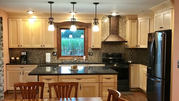 A modern kitchen with wooden cabinets, a black refrigerator, and a large island with chairs.