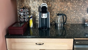 A kitchen with wooden cabinets, a coffee maker, a kettle, and a coffee grinder on the counter.