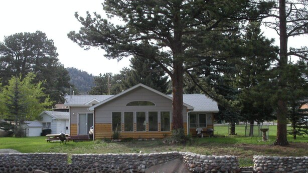 A cabin with a stone retaining wall in front, a picnic table, and a large tree nearby.