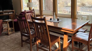 A dining area with a large table, wooden chairs, and a television in the background.