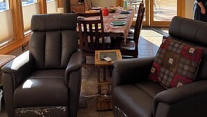 A dining area with a table set for four, surrounded by leather chairs. There is a wooden cabinet against the wall, a clock, and a window with blinds.