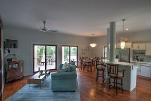 Amplia sala de estar con sofá, comedor con sillas de madera y cocina con armarios blancos y refrigerador.