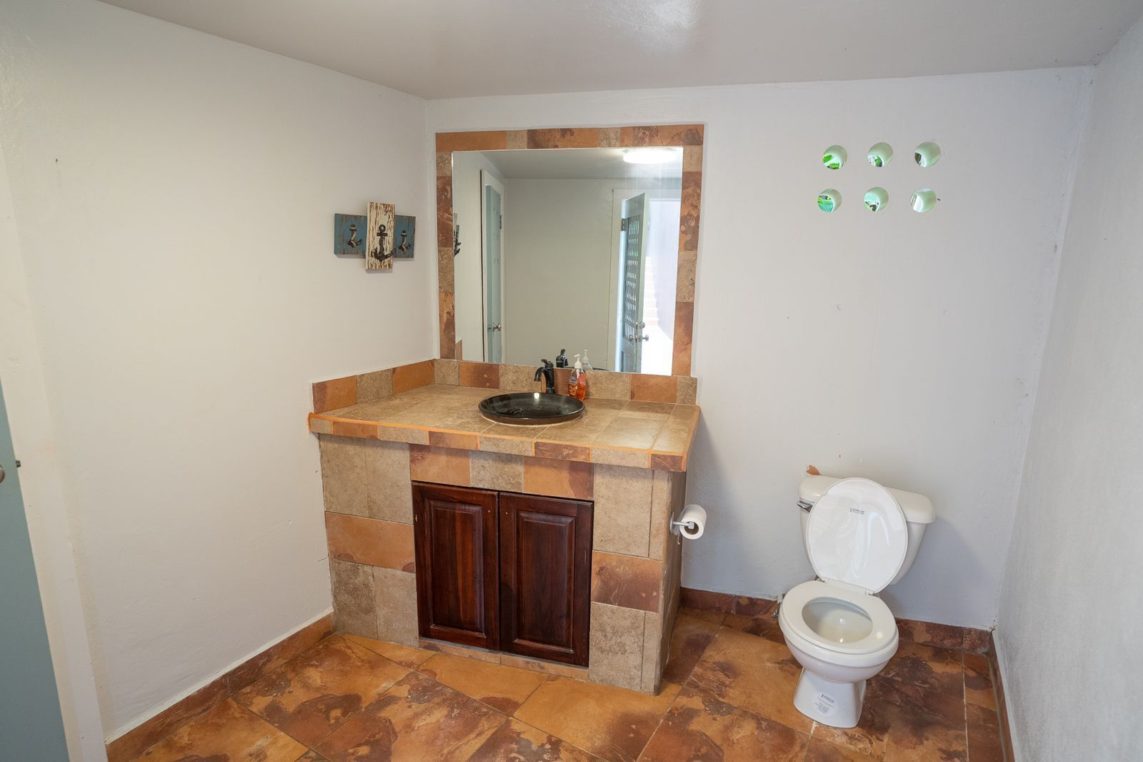 Ein Badezimmer mit einem Becken aus Stein, Holzschränken, einer Toilette und einem Spiegel.