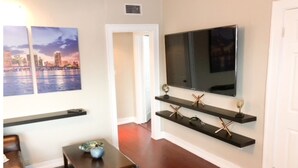 Ein Wohnzimmer mit Flachbildfernseher an der Wand, Holzregalen mit Dekoration, einem Couchtisch und einem Sofa.