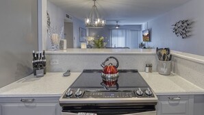 Een keuken met een gasfornuis, oven en een rode waterkoker op het aanrecht.