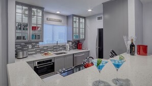 Een moderne keuken met een ingebouwde vaatwasser, een roestvrijstalen broodrooster en een magnetron. Op het aanrecht staan twee martini-glazen met blauwe drank.