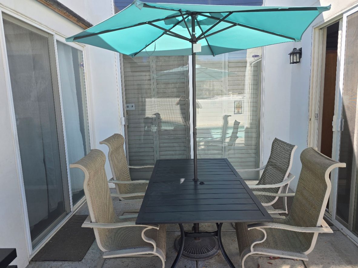 Une terrasse avec une table et quatre chaises, un parasol et une porte moustiquaire.