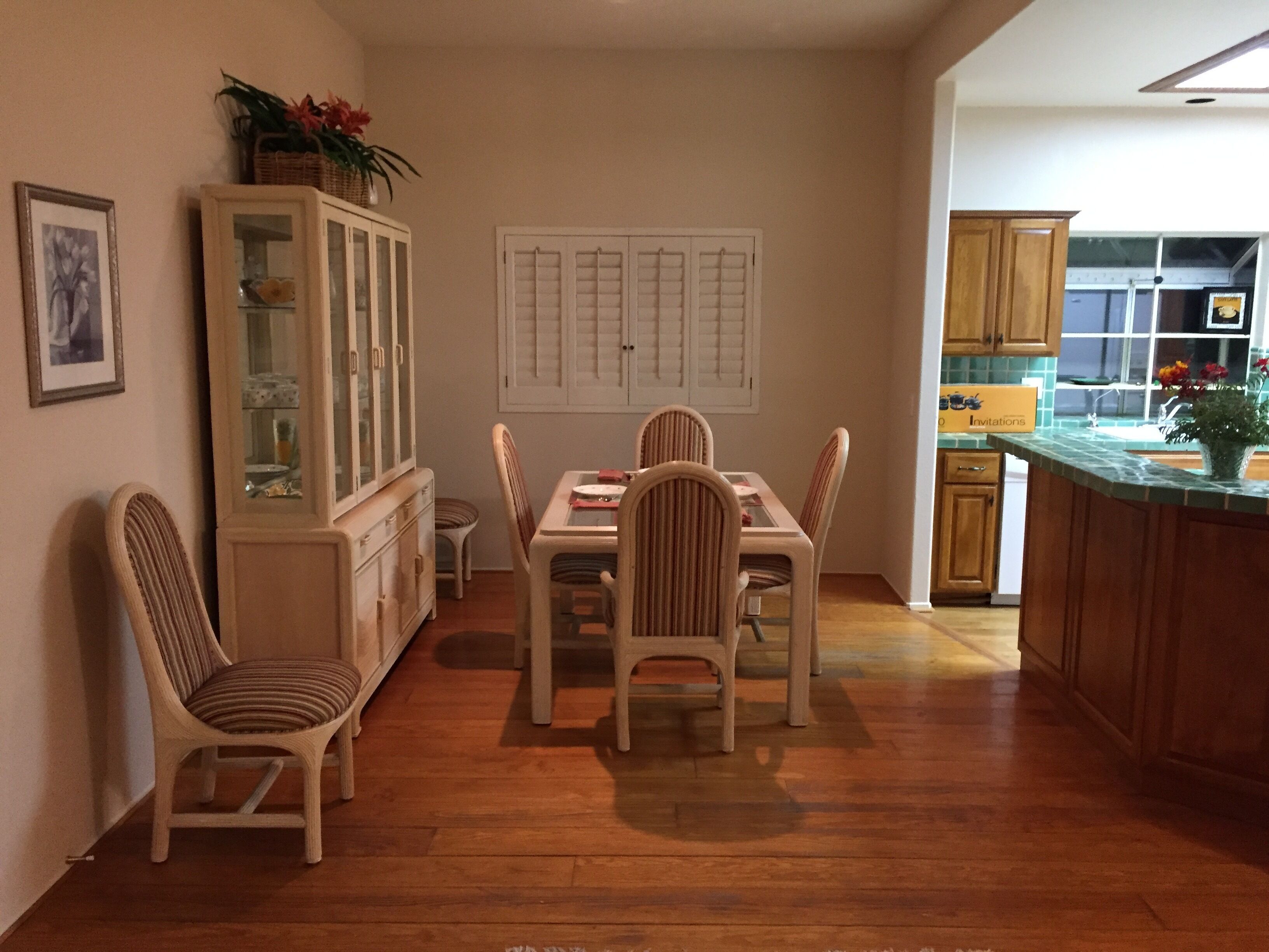 Un comedor con una mesa y sillas de madera, un aparador con puertas de cristal y una cocina visible a través de una puerta abierta.