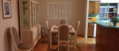 Un comedor con una mesa y sillas de madera, un aparador con puertas de cristal y una cocina visible a través de una puerta abierta.