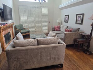 A living room with a fireplace, two sofas, a television, and a window with blinds.