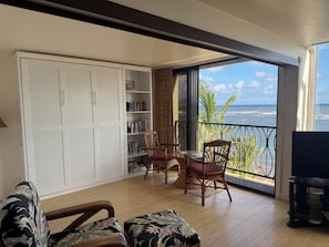 A balcony with a view of the ocean, a white wardrobe, and a seating area with a table and chairs.