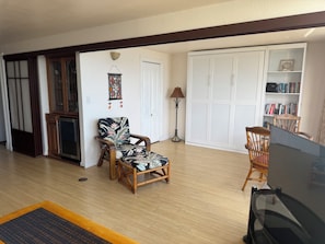A living room with a wooden floor, a sofa, a chair, a lamp, a bookshelf, and a wardrobe.