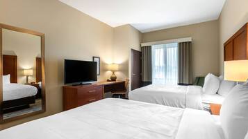 Une chambre d’hôtel avec deux lits, une télévision, un bureau avec une lampe et un grand miroir.