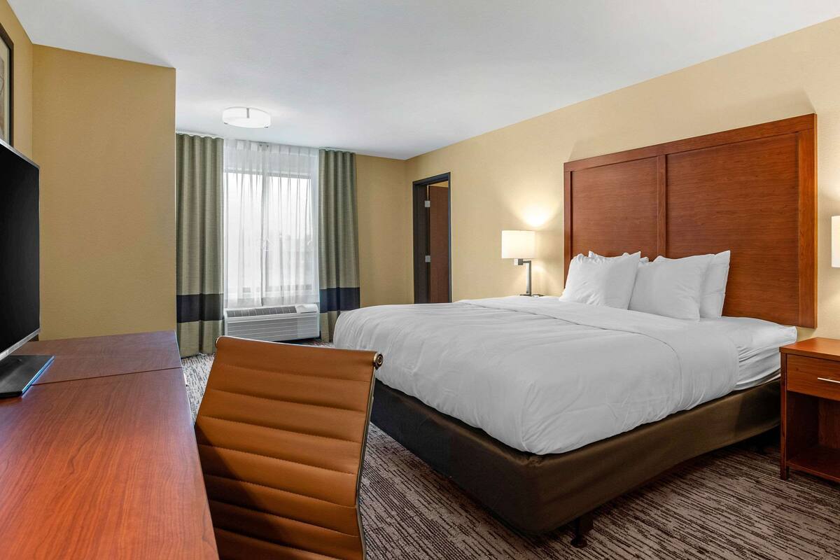 Camera d'albergo con un letto grande, una scrivania, una sedia, una televisione e una finestra con tende.