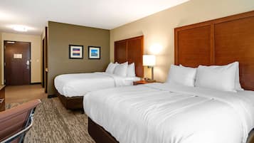 A hotel room with two beds, a wooden headboard, a nightstand with a lamp, and a framed picture on the wall.