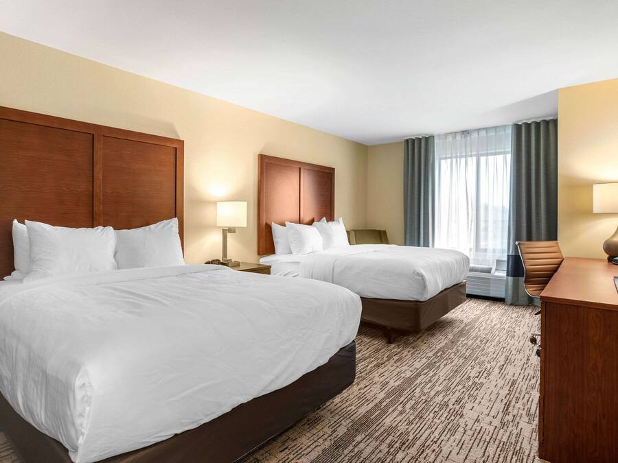 A hotel room with two beds, a desk, a chair, and a TV.
