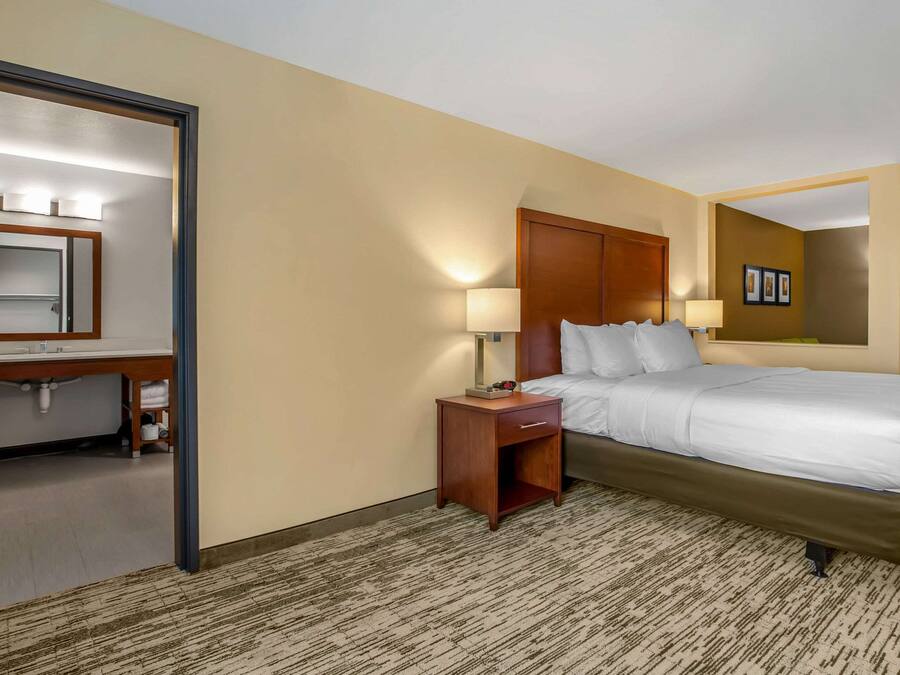 A hotel room with a bed, a nightstand, a mirror, and a wall-mounted lamp.