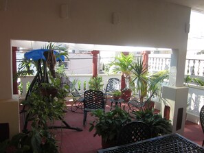 A covered outdoor seating area with potted plants and metal chairs. - Hostal Luly y Rene (Cienfuegos)