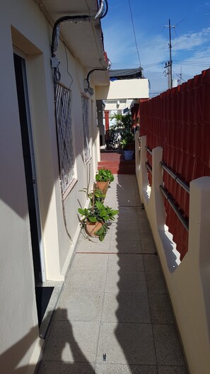 A narrow alleyway with potted plants, a metal gate, and a red fence. - Hostal Luly y Rene (Cienfuegos)