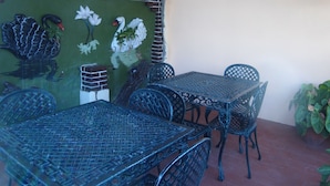 Eine Terrasse mit Tisch und Stühlen, ein Wandgemälde mit Schwänen und Blumen sowie eine Ziegelwand.